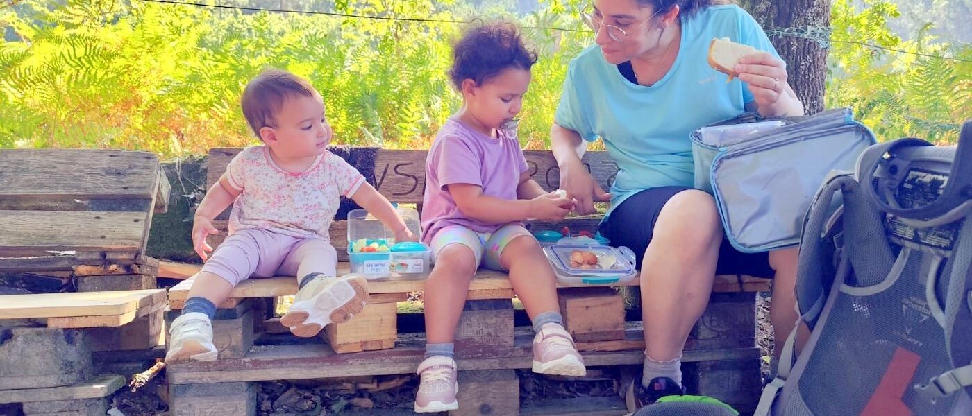 אם ושתי פעוטות אוכלות ארוחת צהריים על ספסל עץ בקמינו
