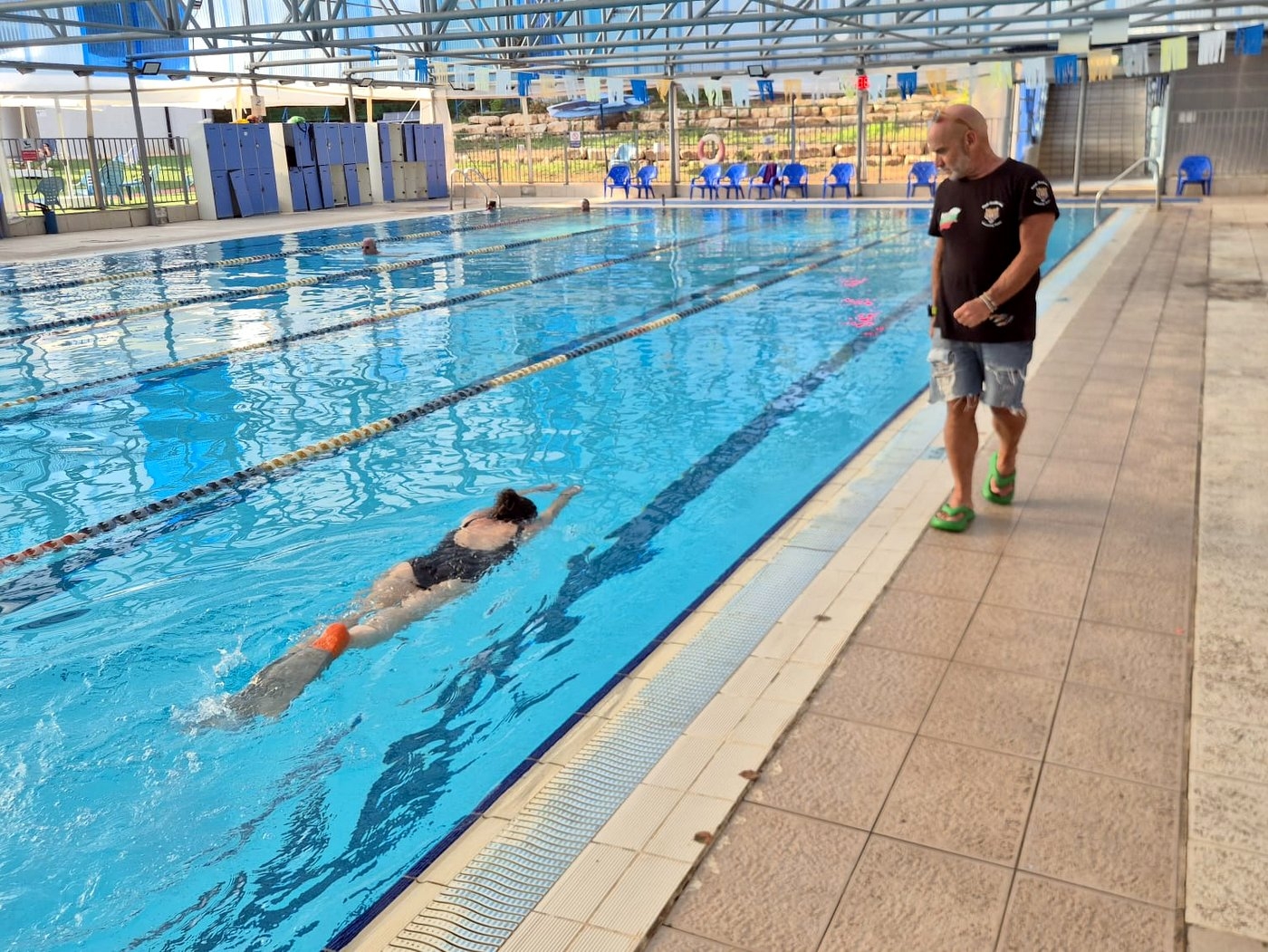 מאמן שחייה צועד לצד הבריכה ומלווה שחיינית בשחיית חתירה
