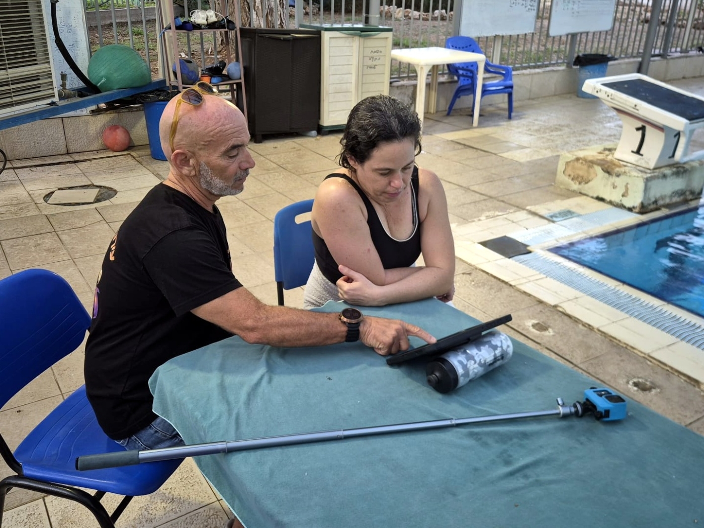 מאמן ושחיינית צופים בטאבלט בניתוח וידאו של טכניקת שחייה