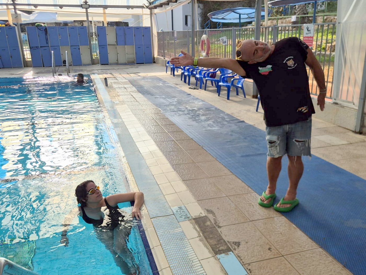 מאמן שחייה מדגים תנועת יד בחתירה לשחיינית שנשענת על דופן הבריכה