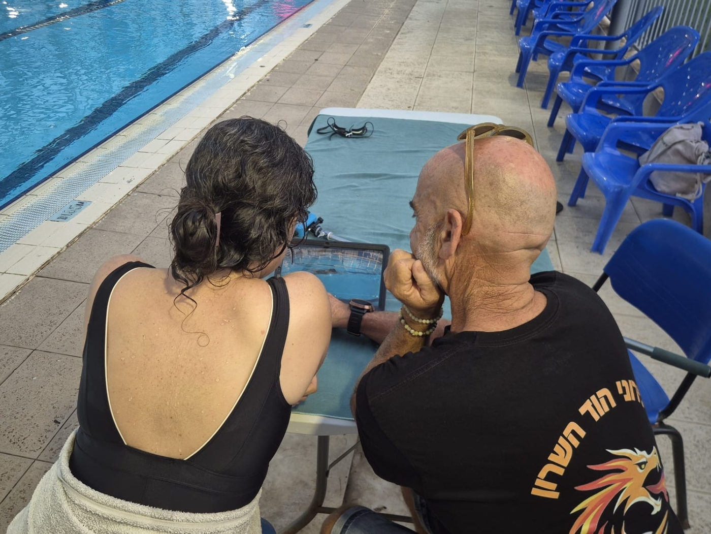 שחיינית ומאמן צופים מגב בצילום וידאו תת-מימי על טאבלט ליד הבריכה