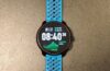 שעון Suunto Race 2 עם רצועה כחולה מונח על משטח בהיר, מסך שעון ראשי
