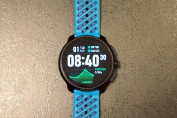 שעון Suunto Race 2 עם רצועה כחולה מונח על משטח בהיר, מסך שעון ראשי