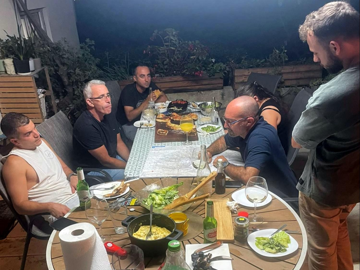 ארוחת ערב קבוצתית בחצר עם מפת טיול לתכנון הטרק באולימפוס